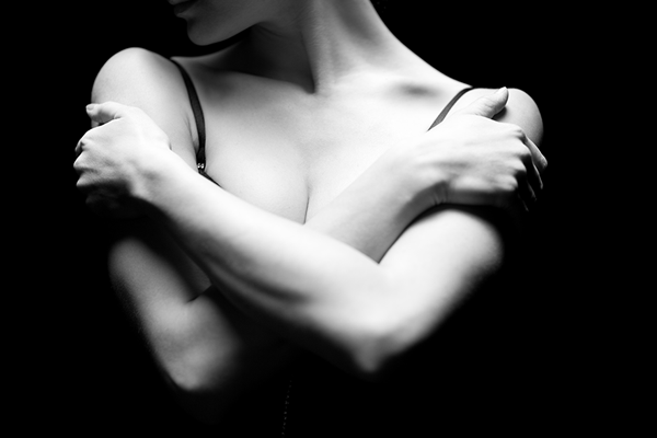Black and white photo of a woman crossing her arms over her breasts and clutching her shoulders
