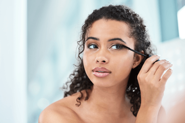 Beautiful African American woman applying mascara while looking into a mirror