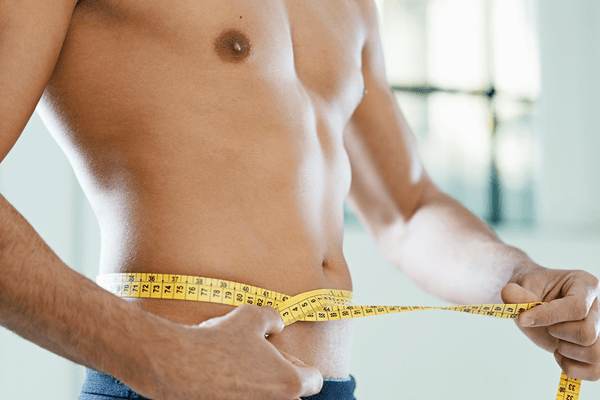 Man measuring his fit abdomen with a measuring tape