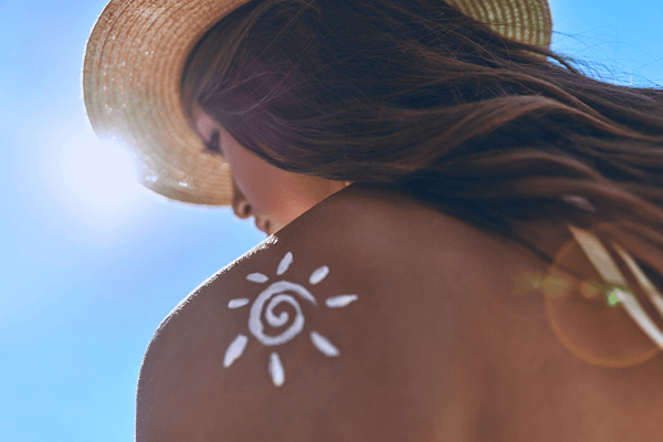 Rear view of the back of a woman in a bikini at the beach applying sunscreen to her shoulder