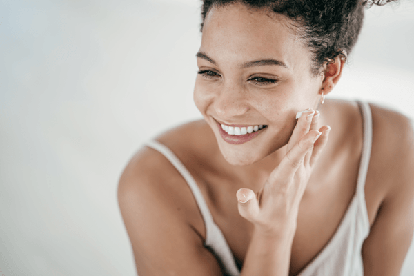 Gorgeous young mixed race woman applying a skincare product to her face while smiling into a mirror